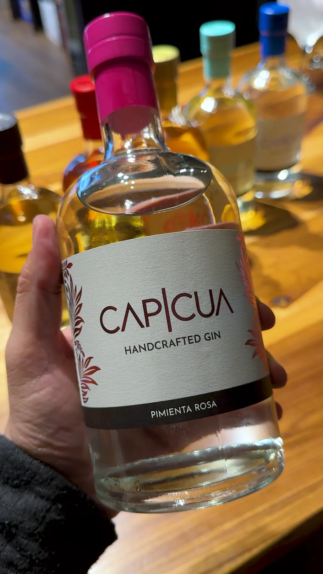 Botella de Pimienta Rosa CAPICÚA sostenida frente a la barra