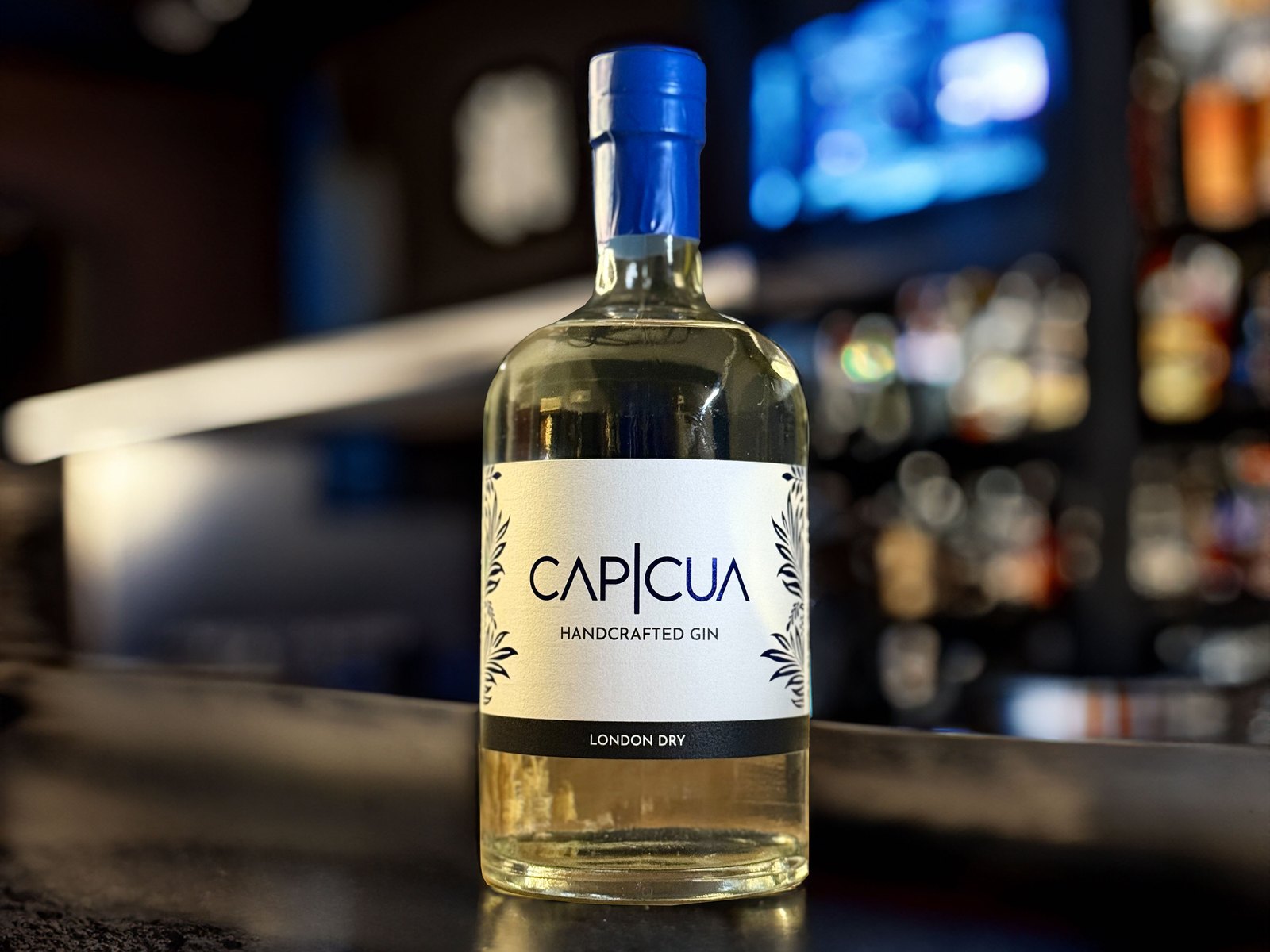 Botella CAPICÚA London Dry en una barra nocturna