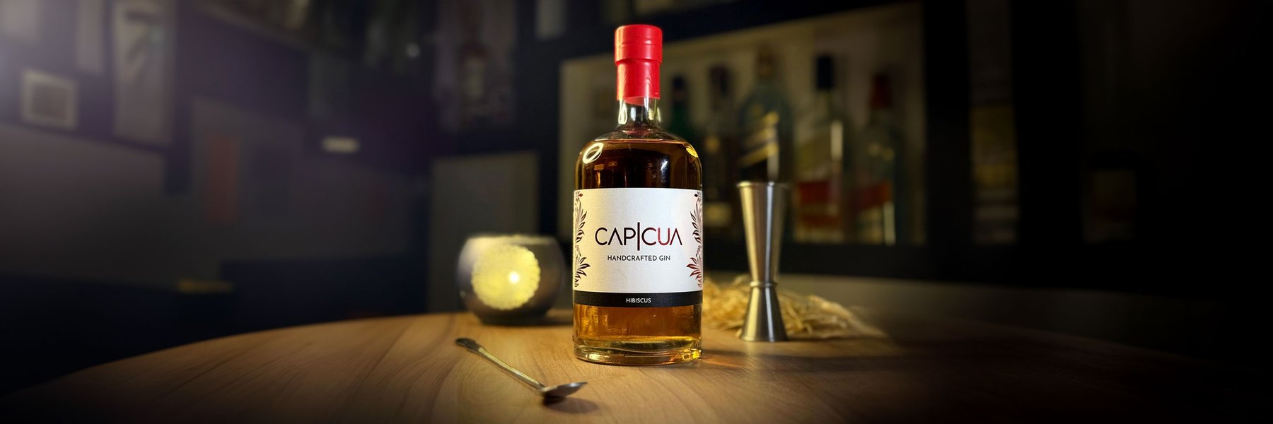 Botella CAPICÚA Hibiscus con jigger y cuchara de bar sobre una barra
