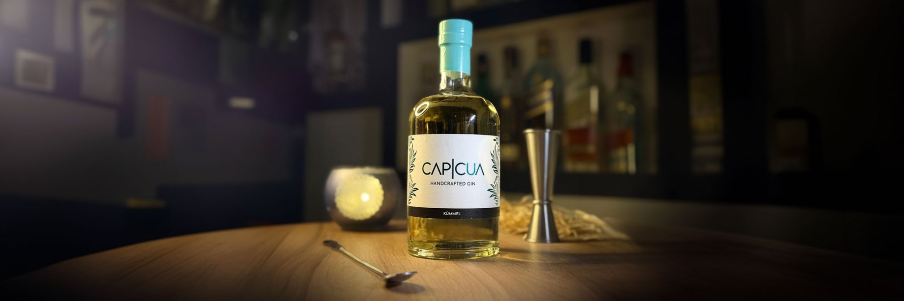 Botella CAPICÚA Kümmel con jigger y cuchara de bar sobre una barra