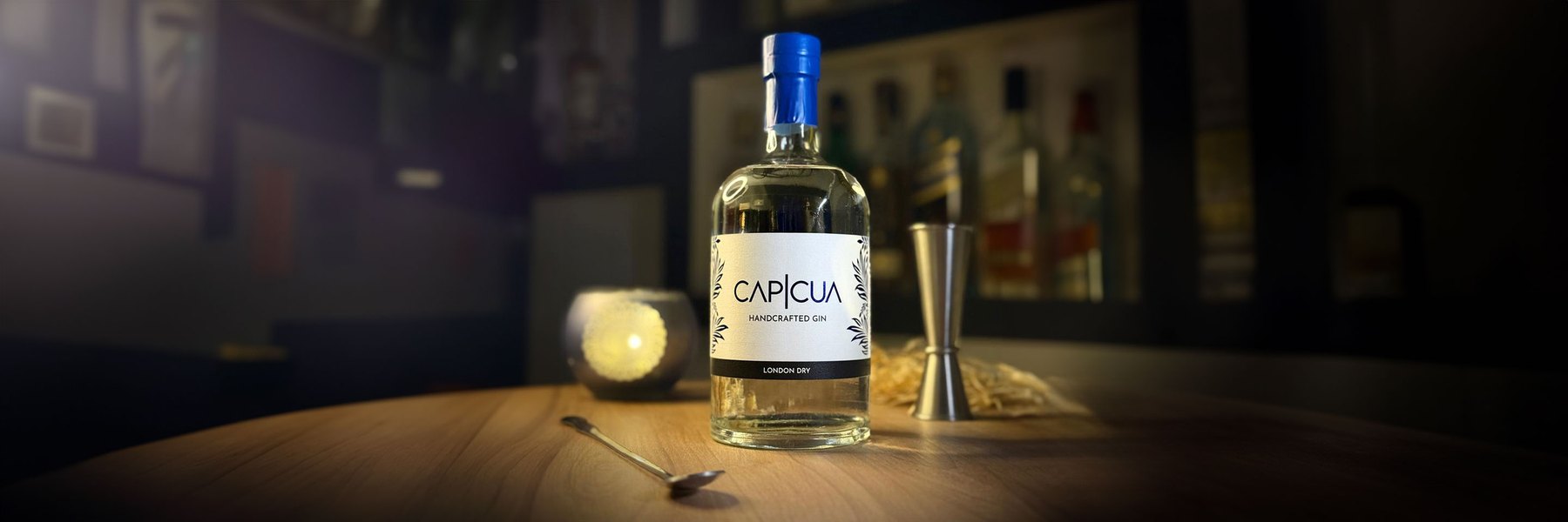 Botella CAPICÚA London Dry con jigger y cuchara de bar sobre una barra