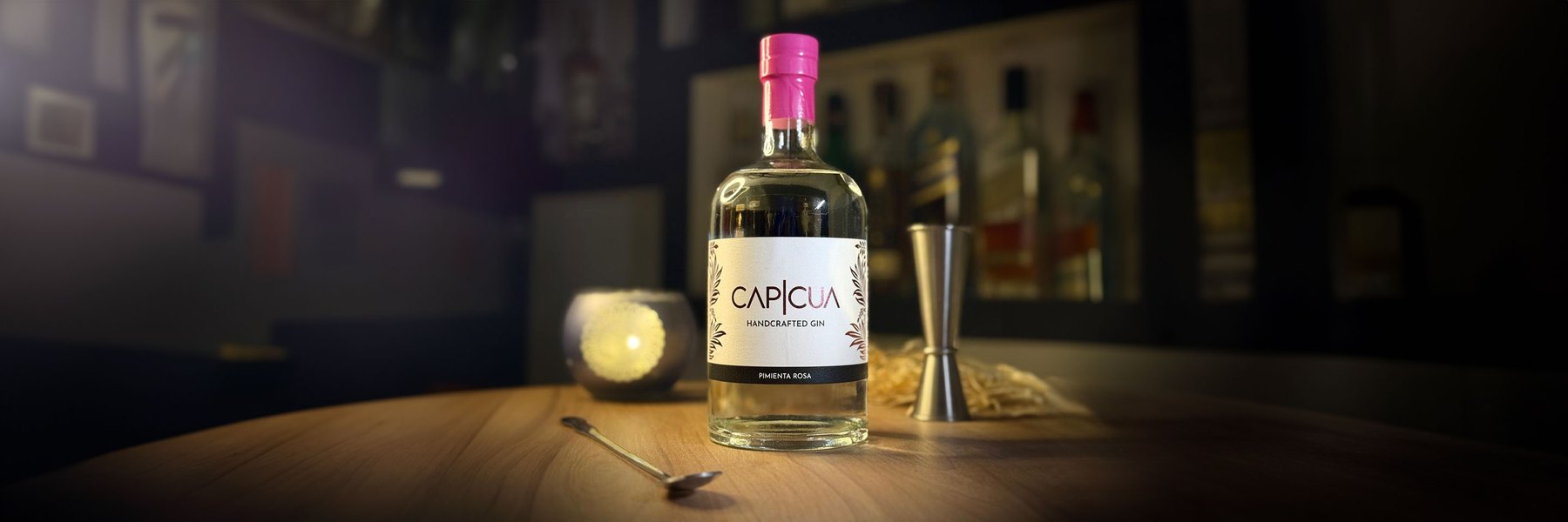 Botella CAPICÚA Pimienta Rosa con jigger y cuchara de bar sobre una barra